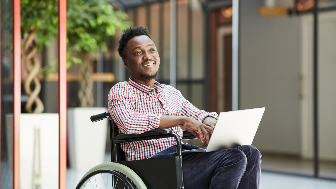 A person using a wheelchair smiles while reviewing financial documents on a laptop.